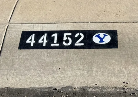 Painted curb address 44152 with a black background, white numbers and a blue BYU logo